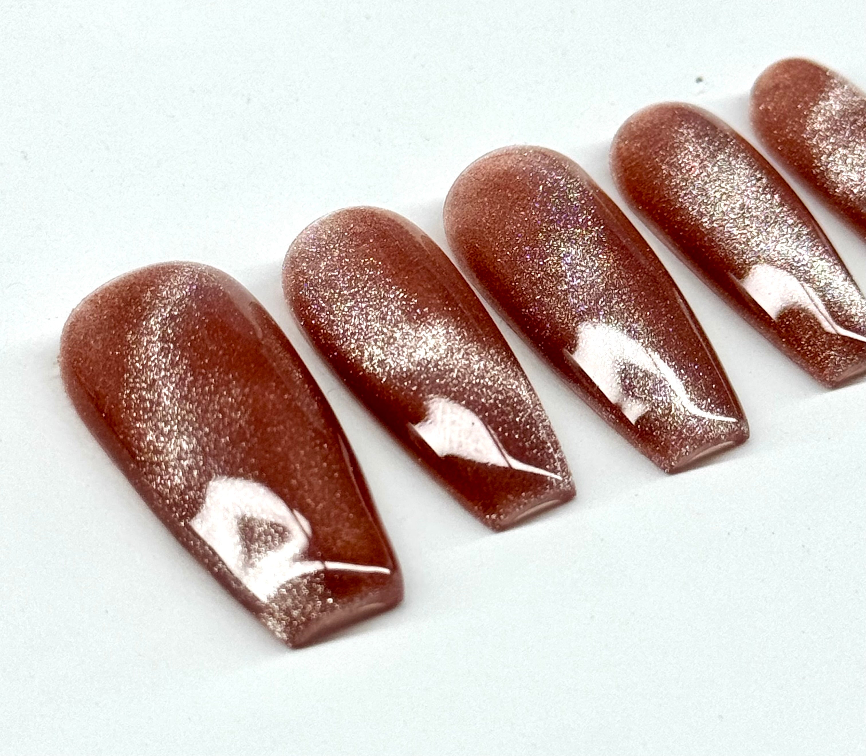 Set of brown glittery nail extensions on a white background
