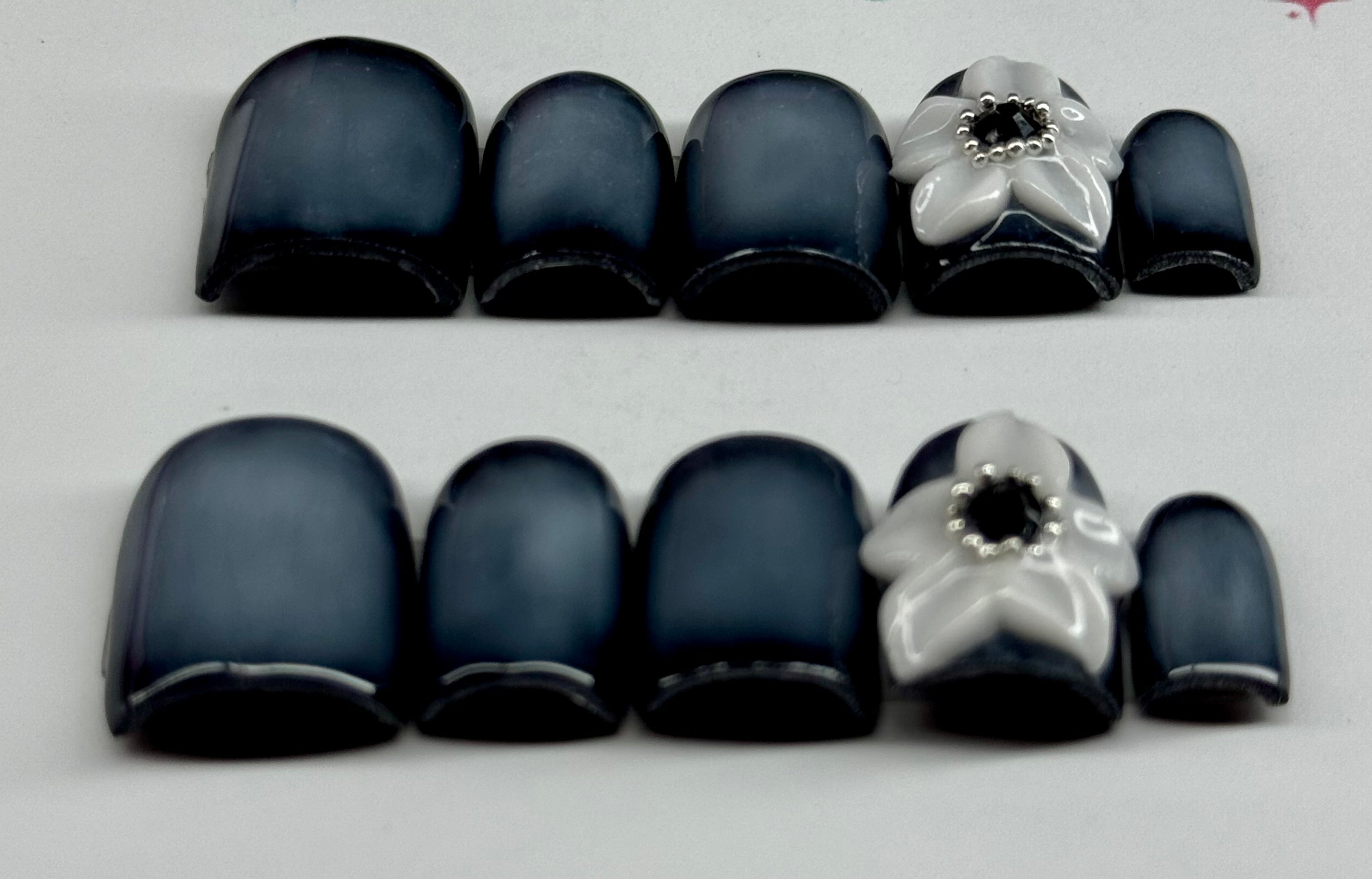 Set of black nail tips with silver flower designs on a light gray background