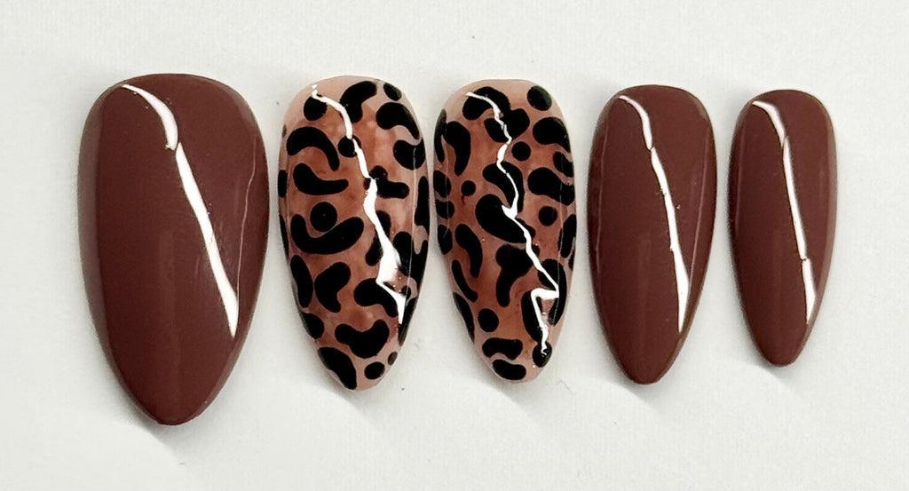 Five brown nail shapes with leopard print and white accents on a light gray background
