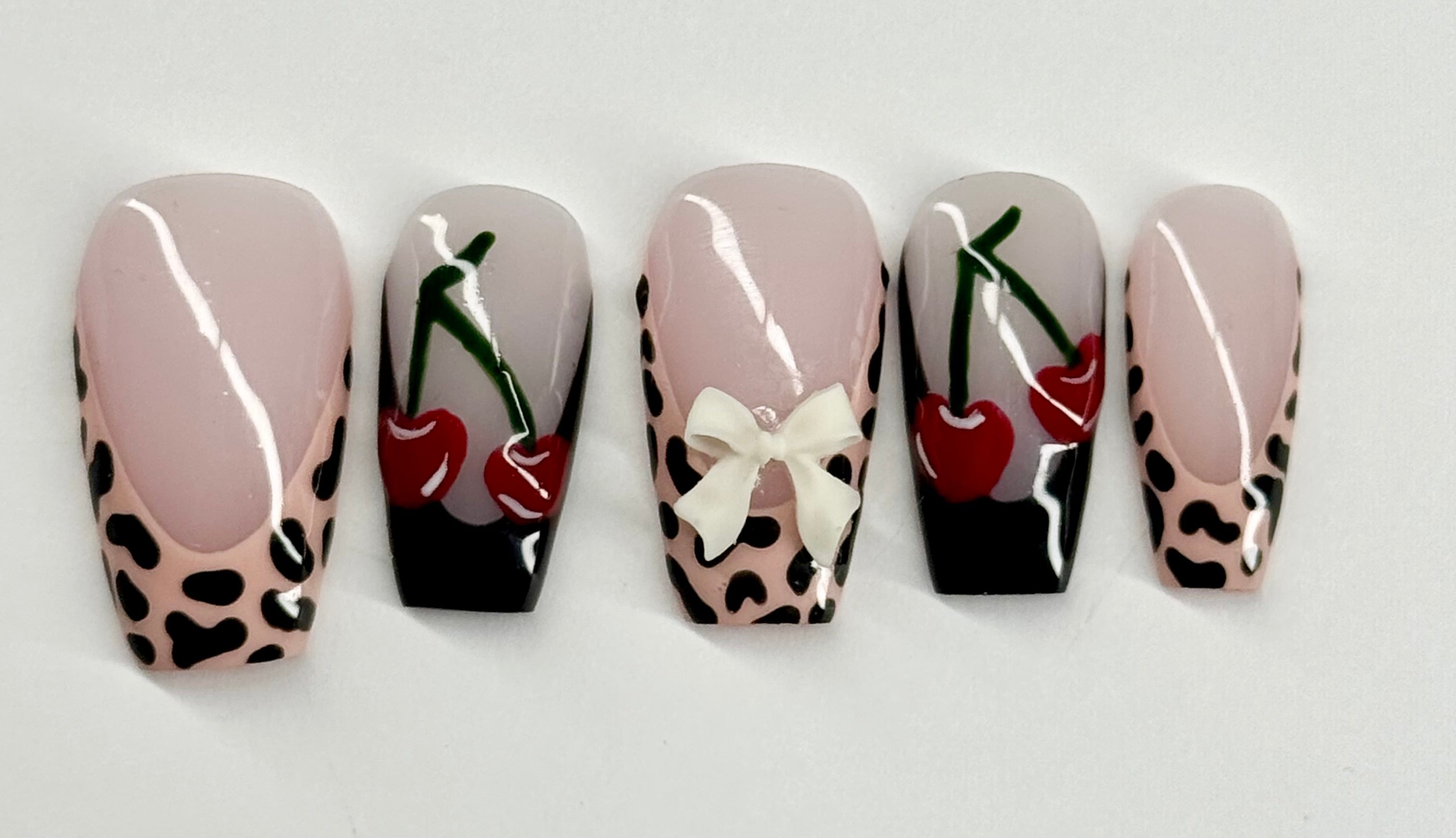 Five nail art designs with cherries and leopard print patterns on a white background