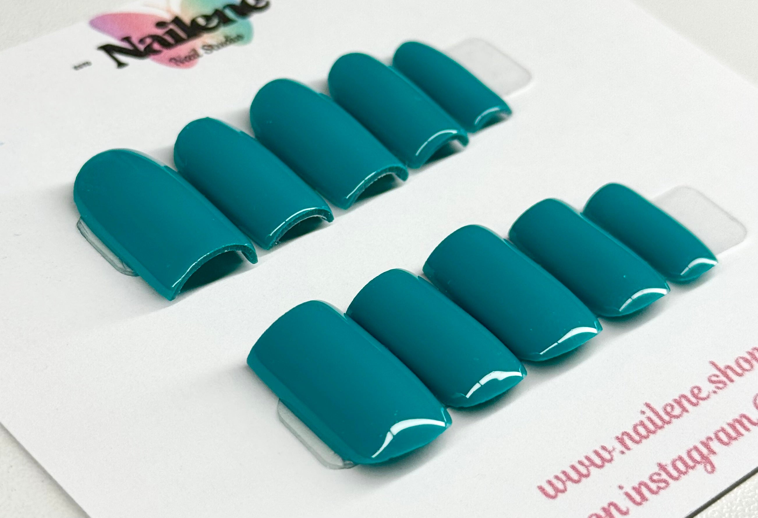 Teal press-on nails on a white card with visible branding.