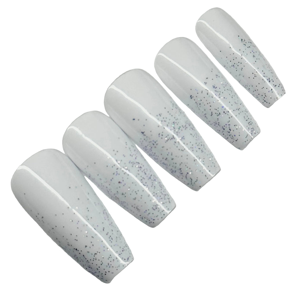 Set of five white nail extensions with black speckles on a light gray background