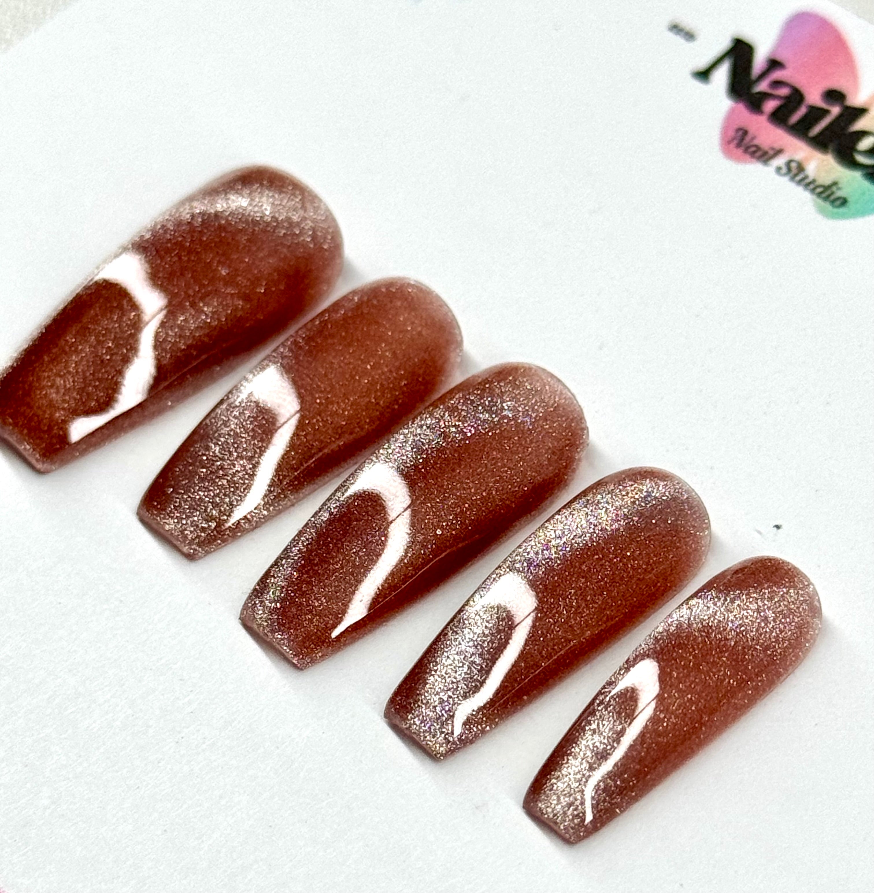 Set of brown glittery nails with white accents on a white background, featuring 'Nail Studio' logo.