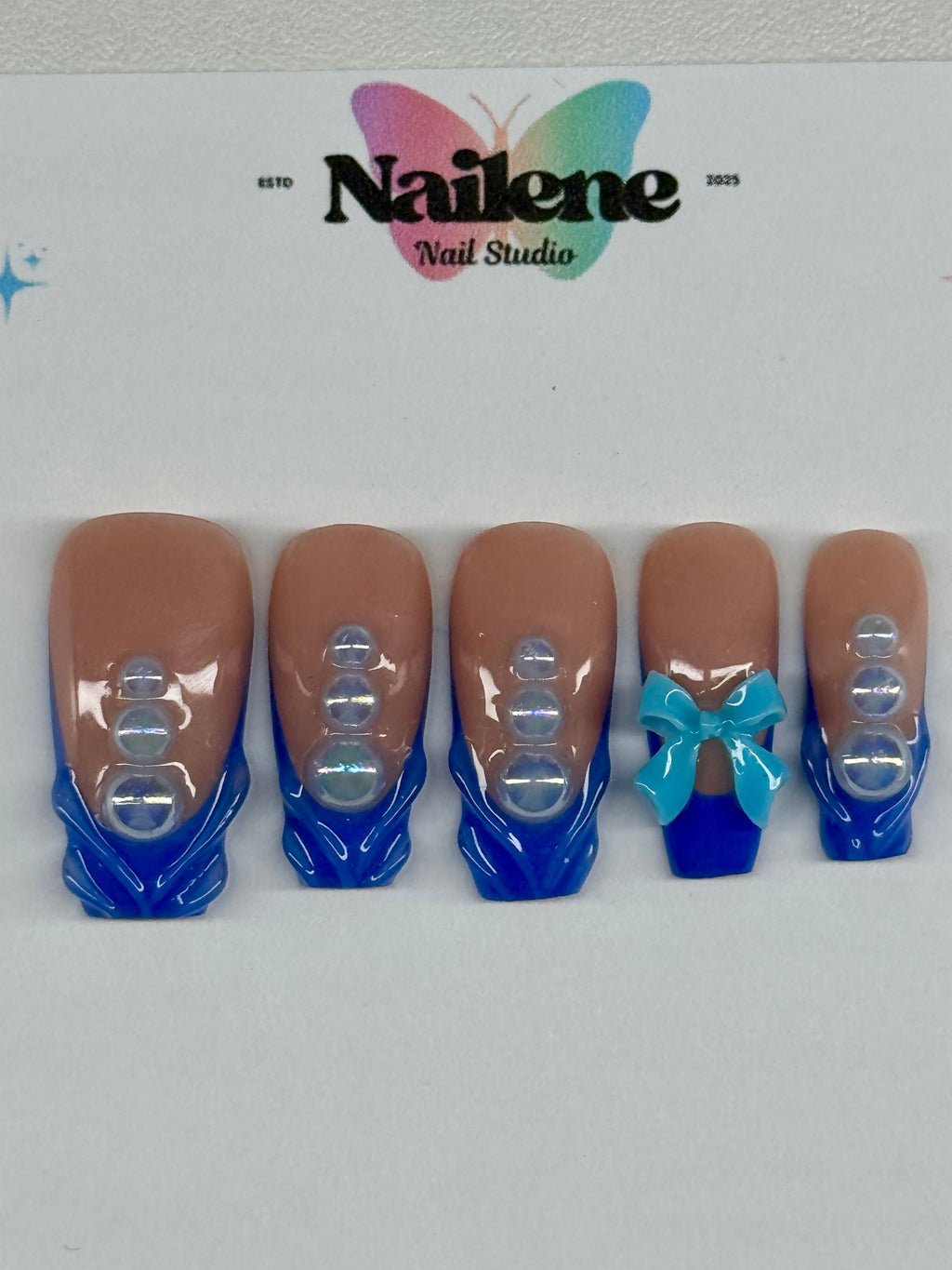 Set of false nails with blue tips and a bow design on a white background with 'Nailene' branding.