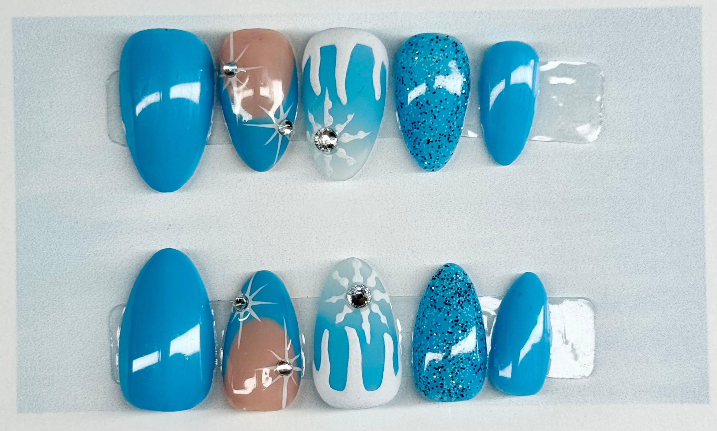 Set of blue, beige, and glittery nail art designs on a gray background