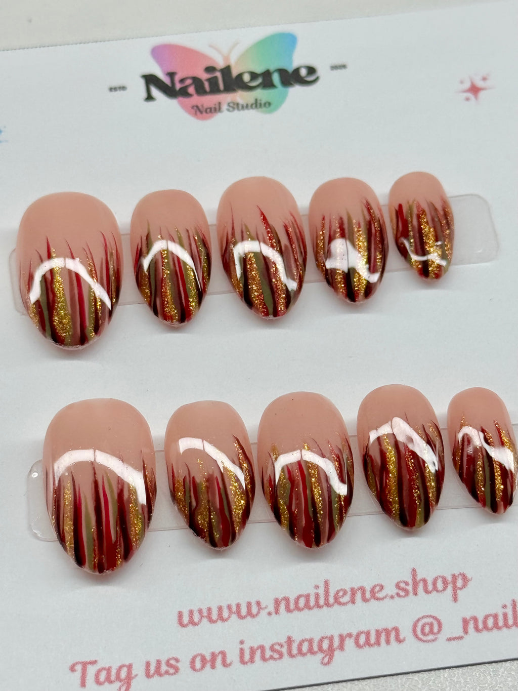 Nail art display with gold and red designs on a clear background, featuring the brand 'Nailene'.