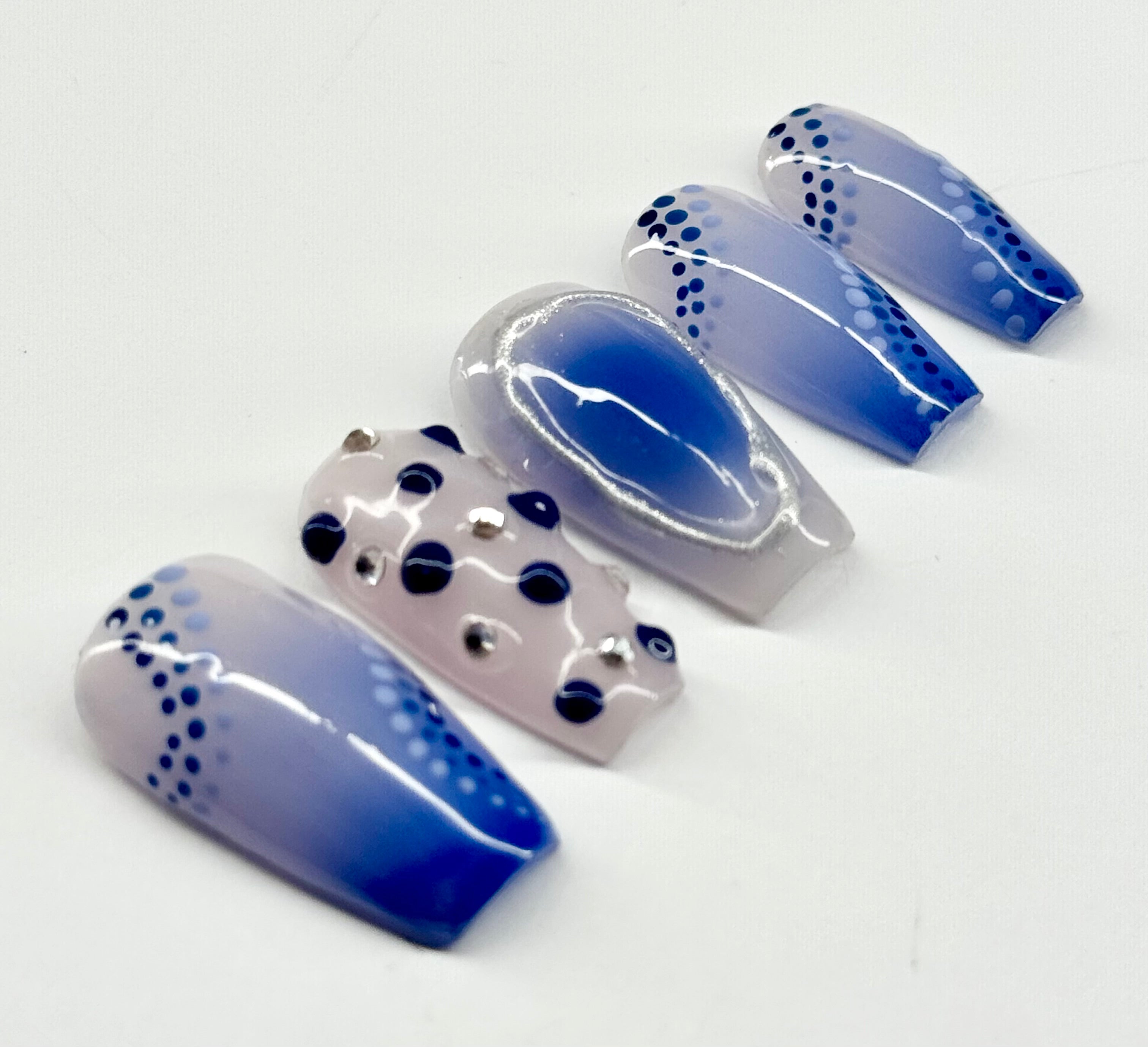 Blue and white nail extensions with black dots on a white background