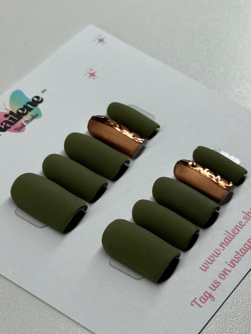 Set of green nail tips with gold accents on a white card.