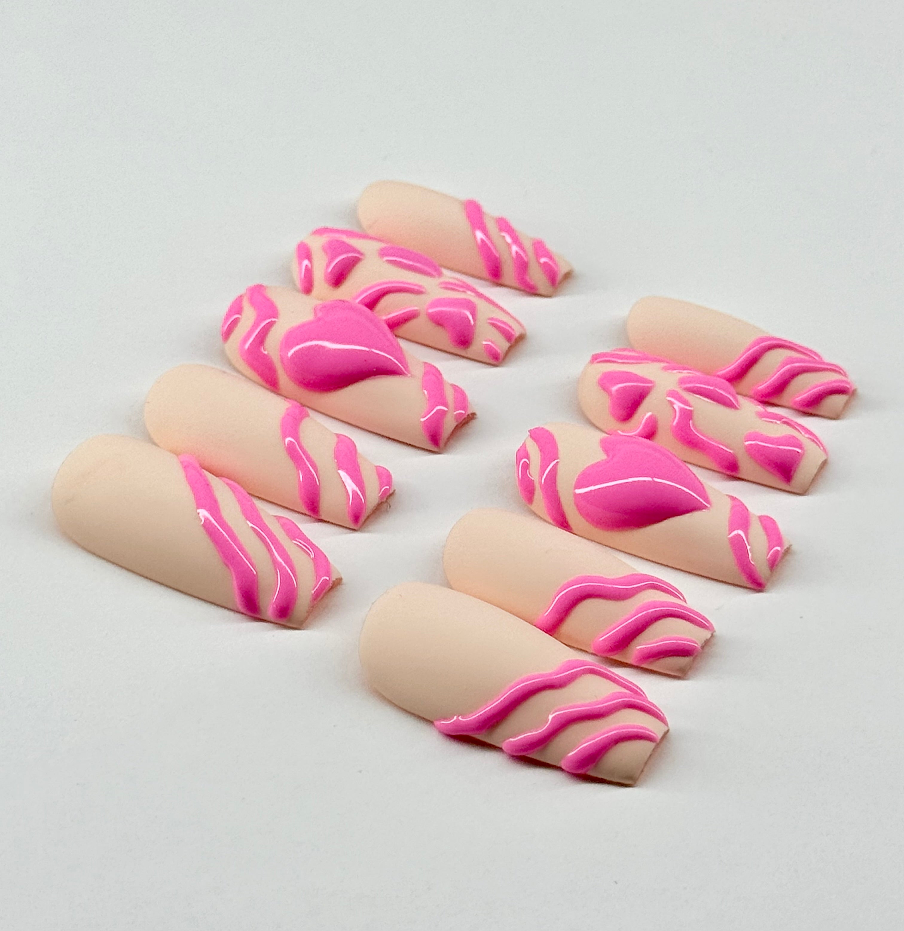 Nail art designs with pink heart patterns on a beige nude background