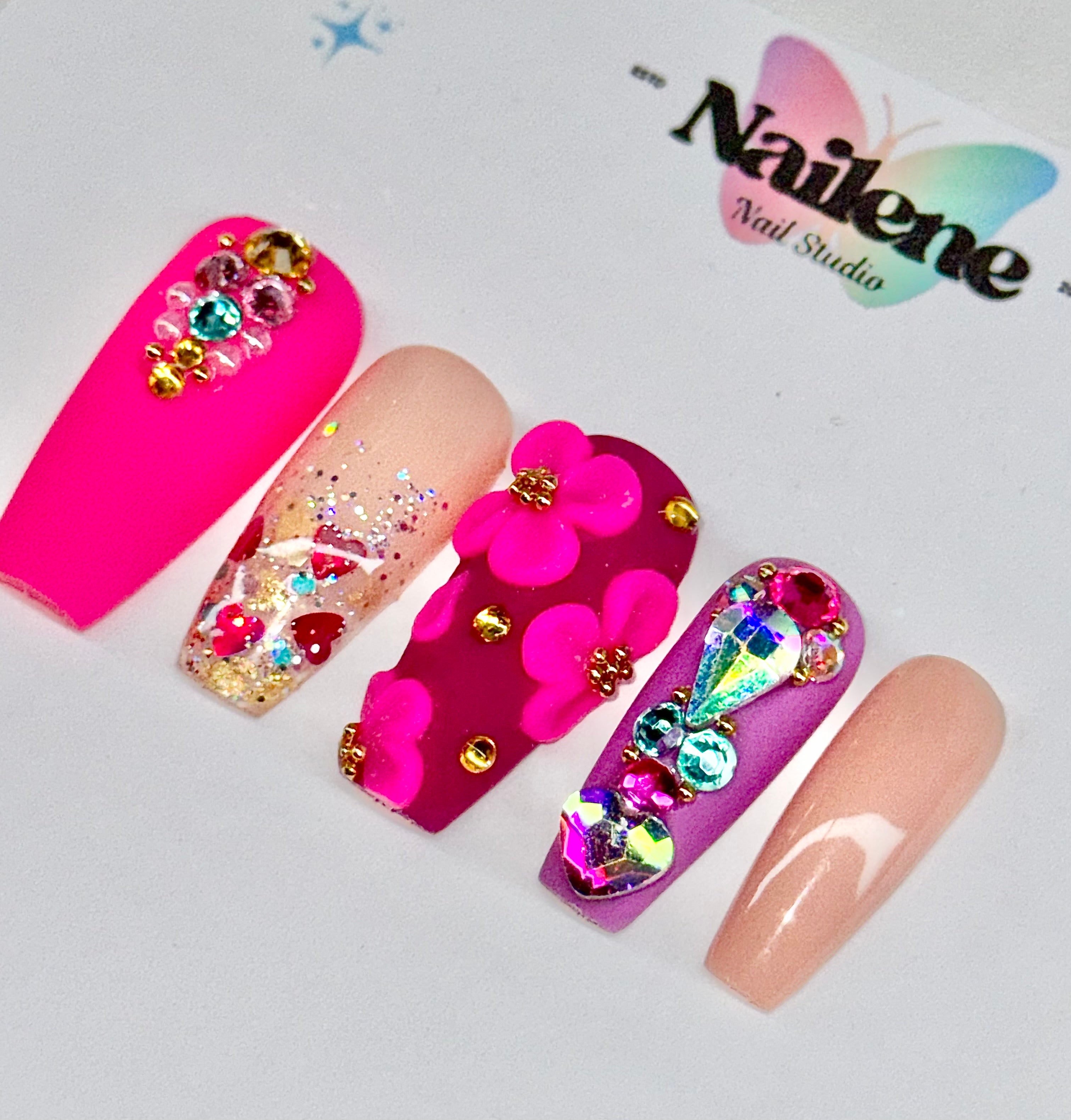 Colorful nail art design with flowers and rhinestones on a white background, featuring the Nailene Nail Studio logo.