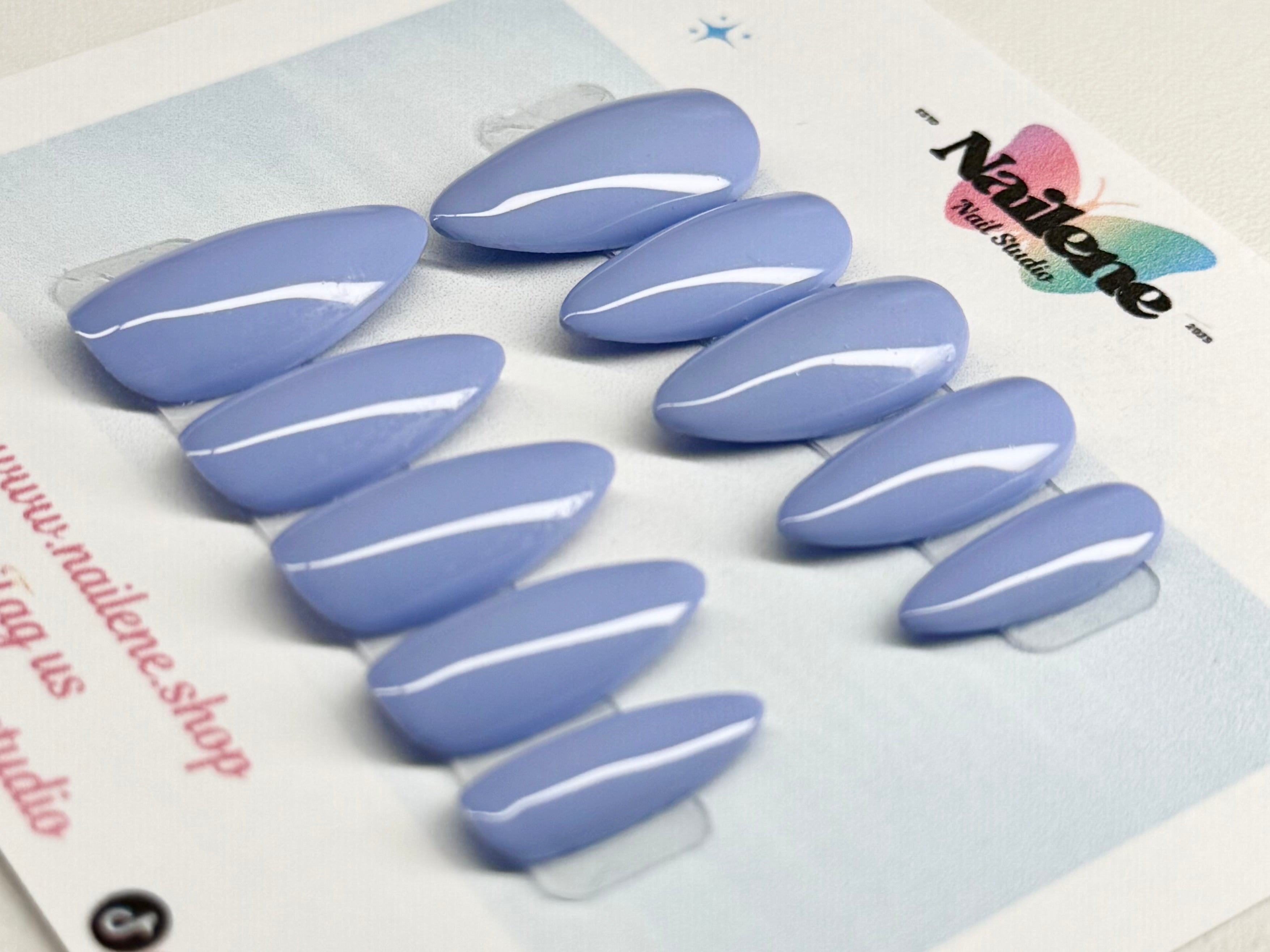 Set of light blue nail extensions with clear top coat against a branded background.
