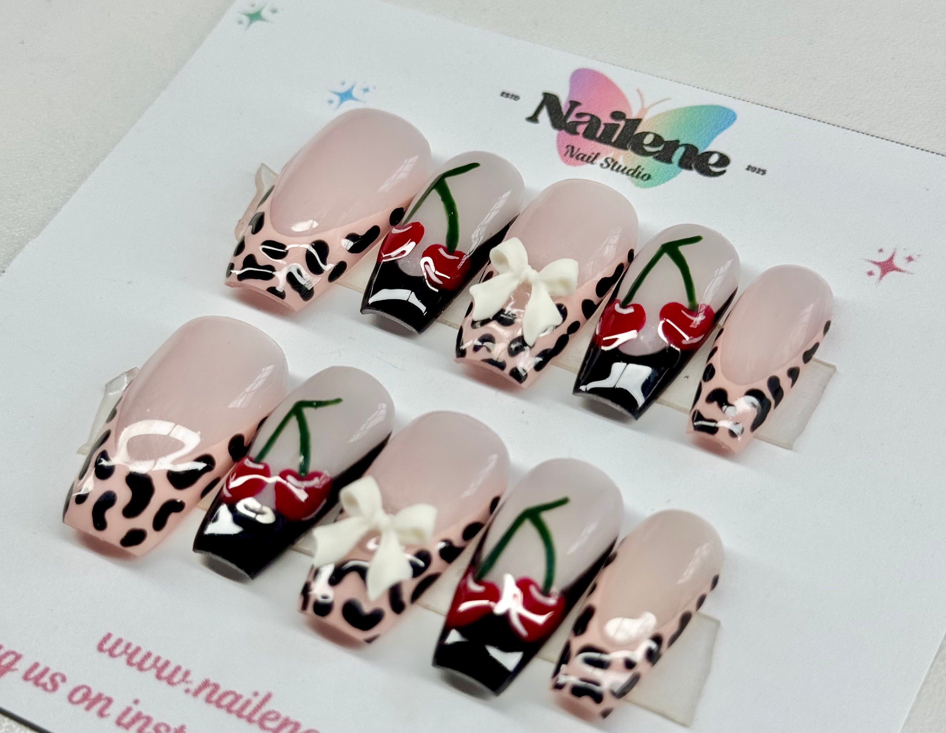 Decorative false nails with leopard print, cherry, and bow design on a white background with 'Nailene' branding.