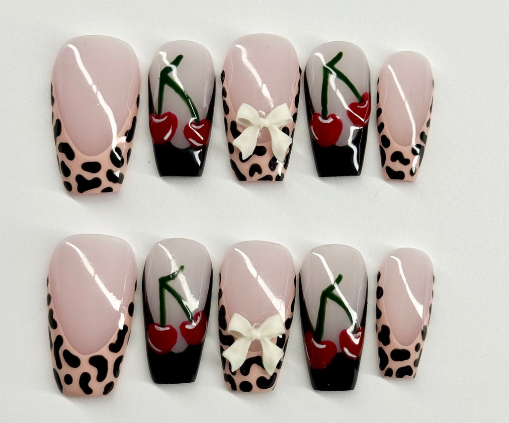 Set of decorative nails with leopard print, cherries, and bows on a white background