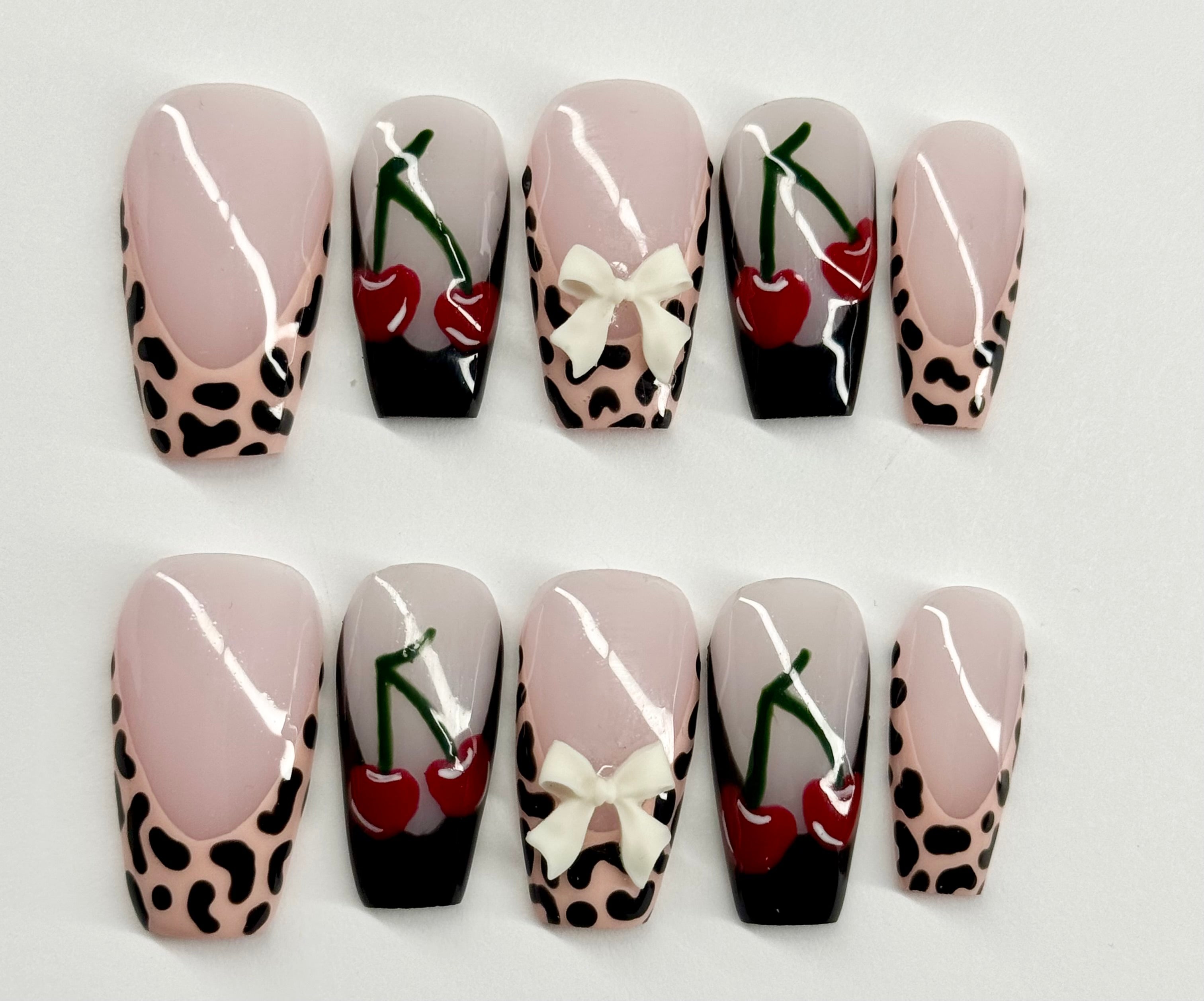 Set of decorative nails with leopard print, cherries, and bows on a white background