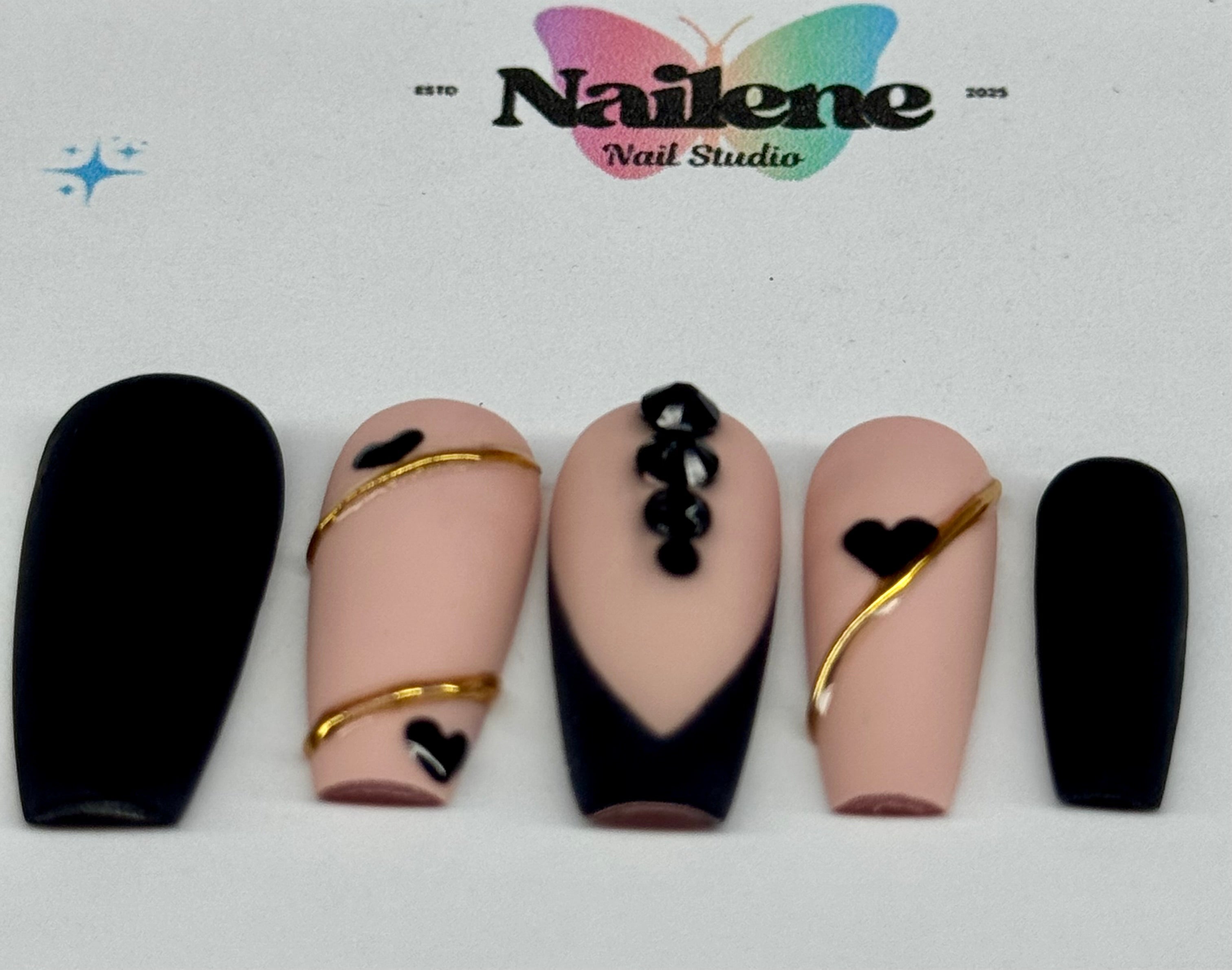 Set of nails with black and gold designs on a white background, featuring the Nailene Nail Studio logo.