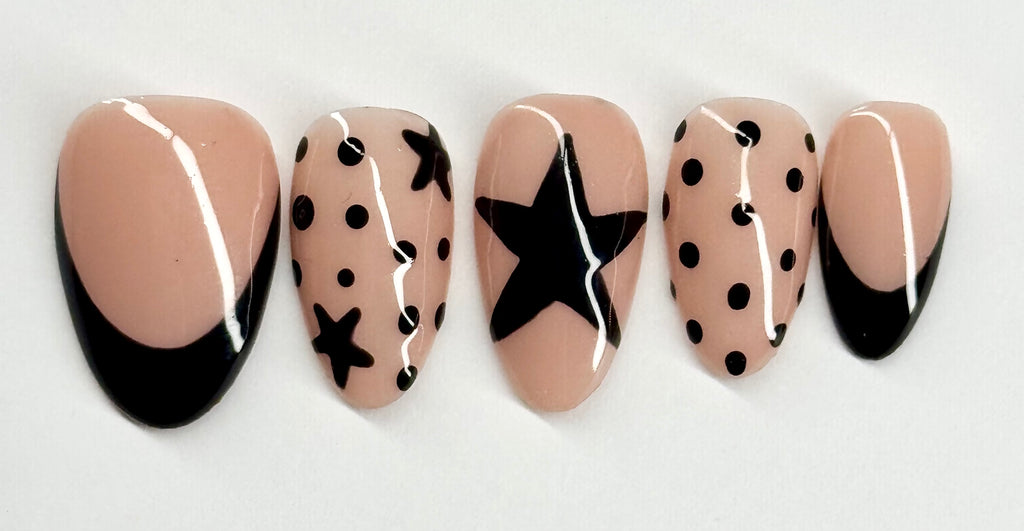 Set of false nails with black star and polka dot designs on a beige background