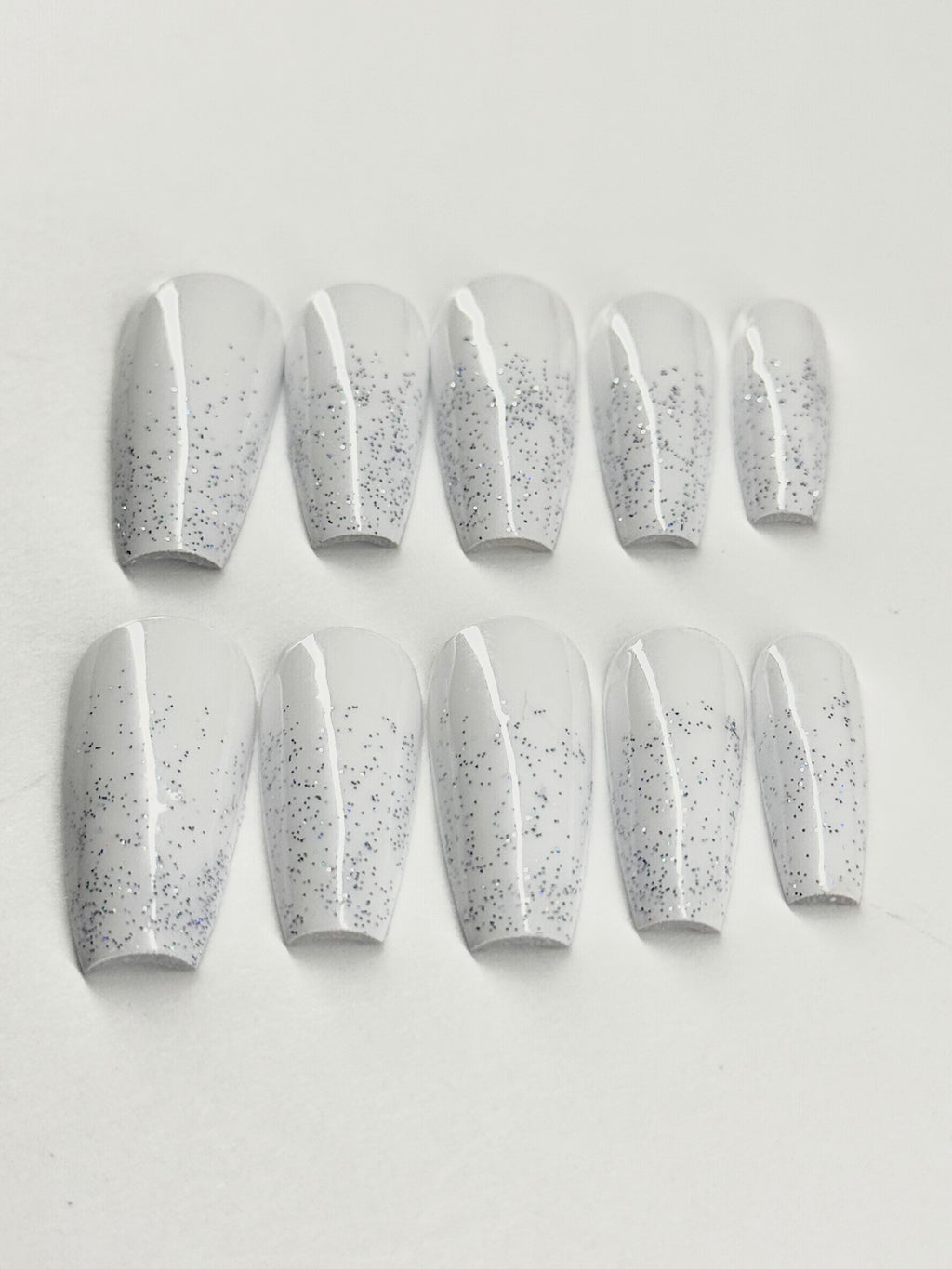 Set of white press-on nails with gray speckles on a light gray background