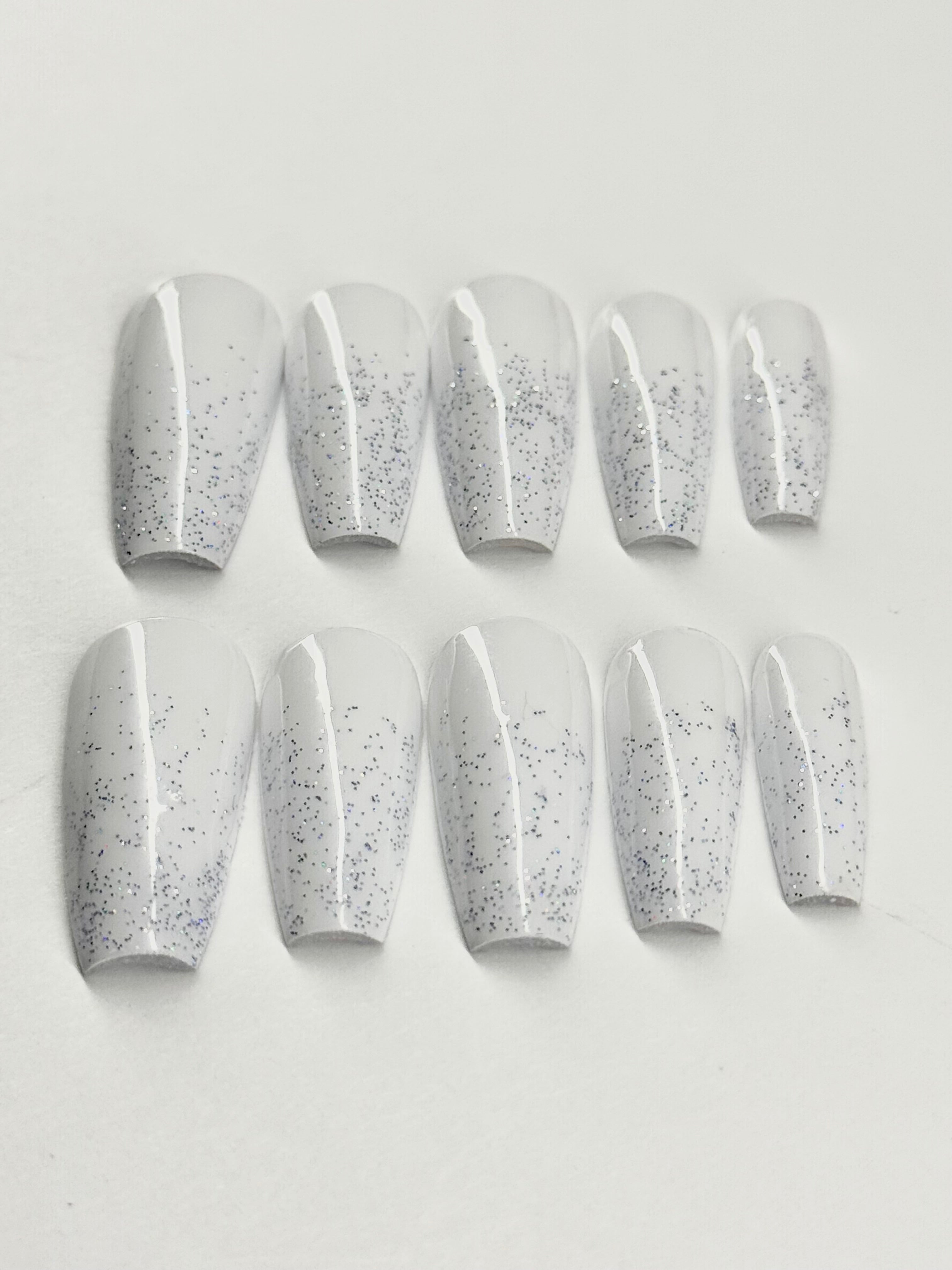 Set of white press-on nails with gray speckles on a light gray background