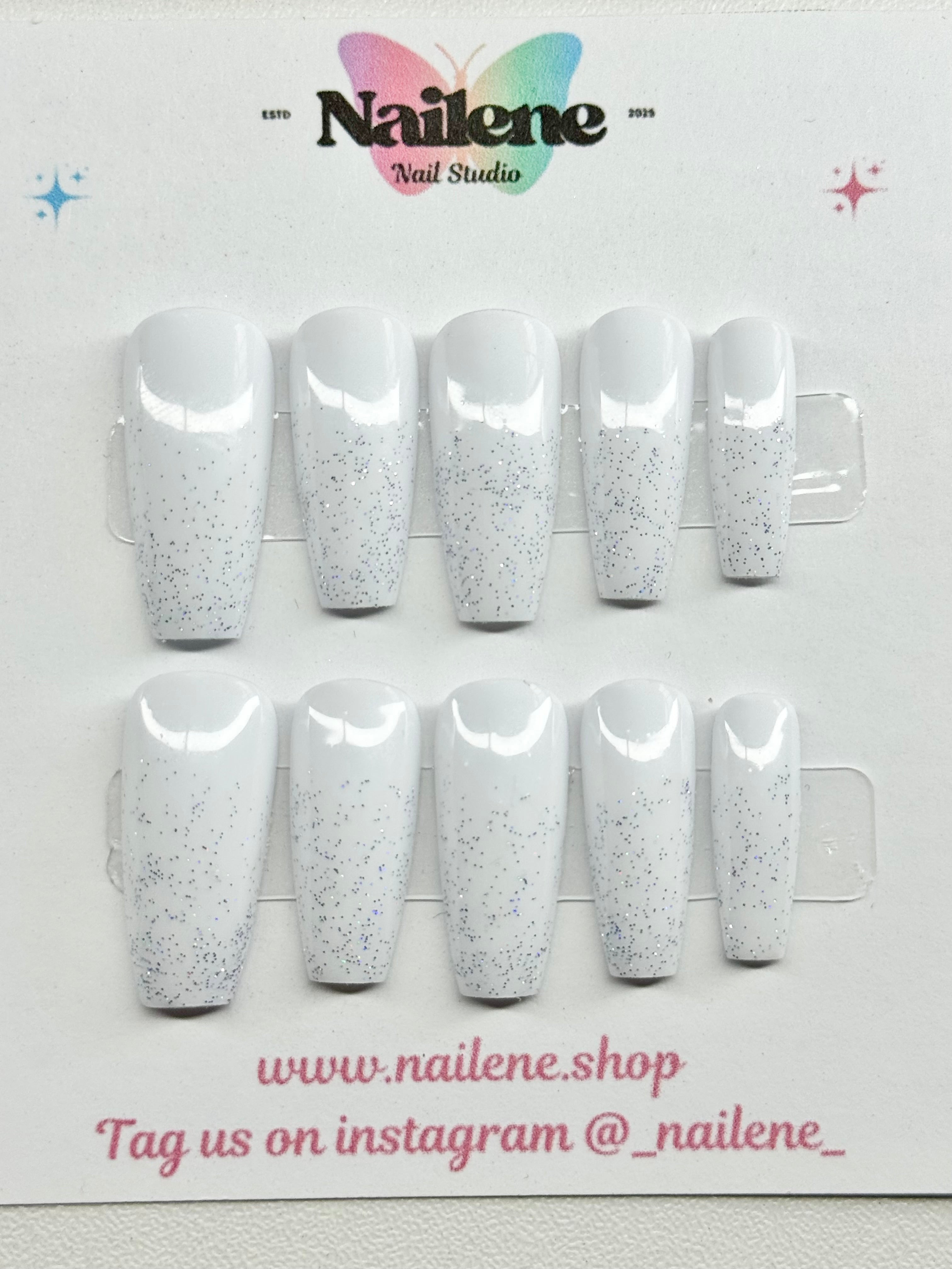 Set of white glittery nail extensions on a display card with Nailene branding.