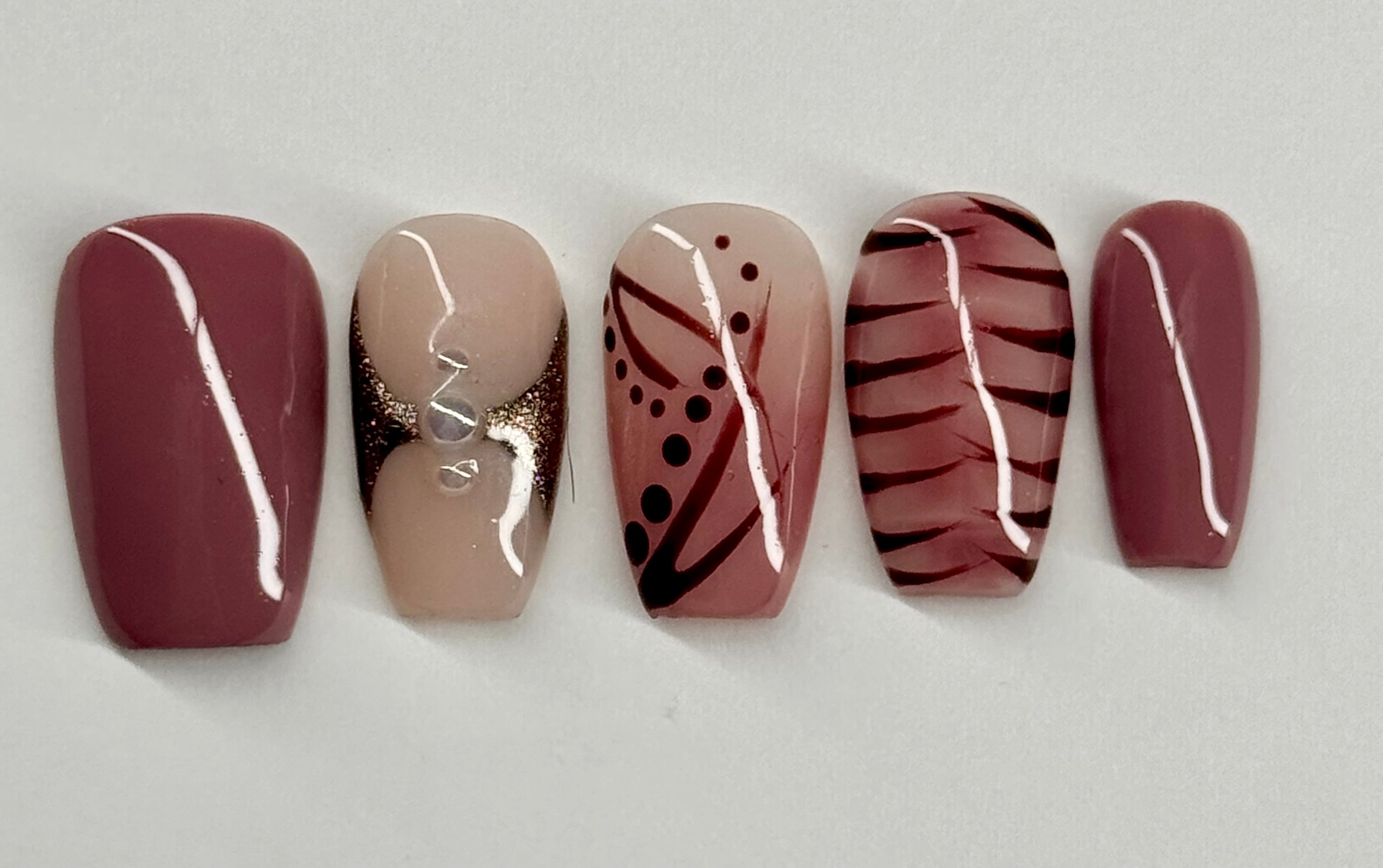 Five nail samples with different designs on a light gray background