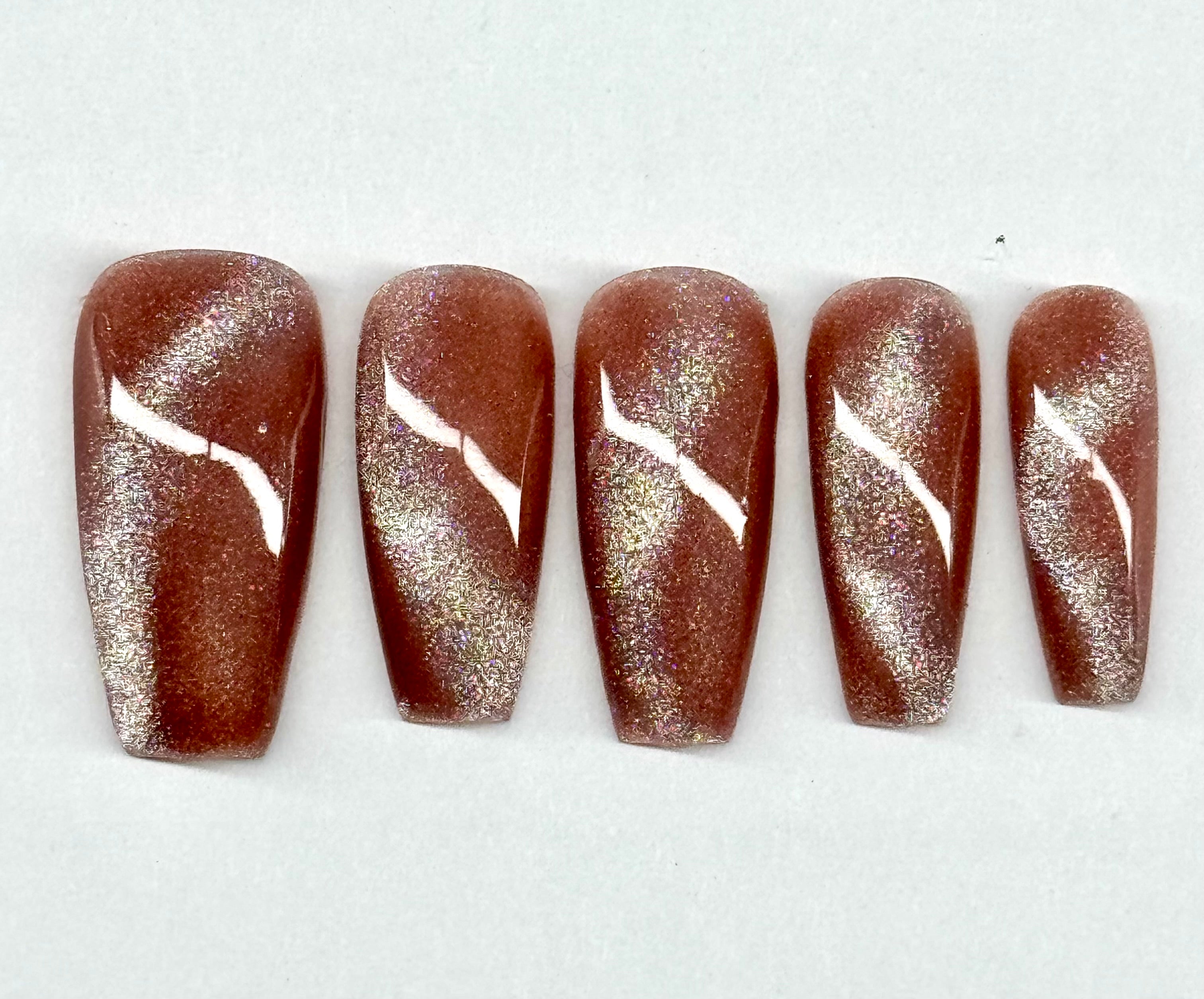 Five brown nail samples with white designs on a white background