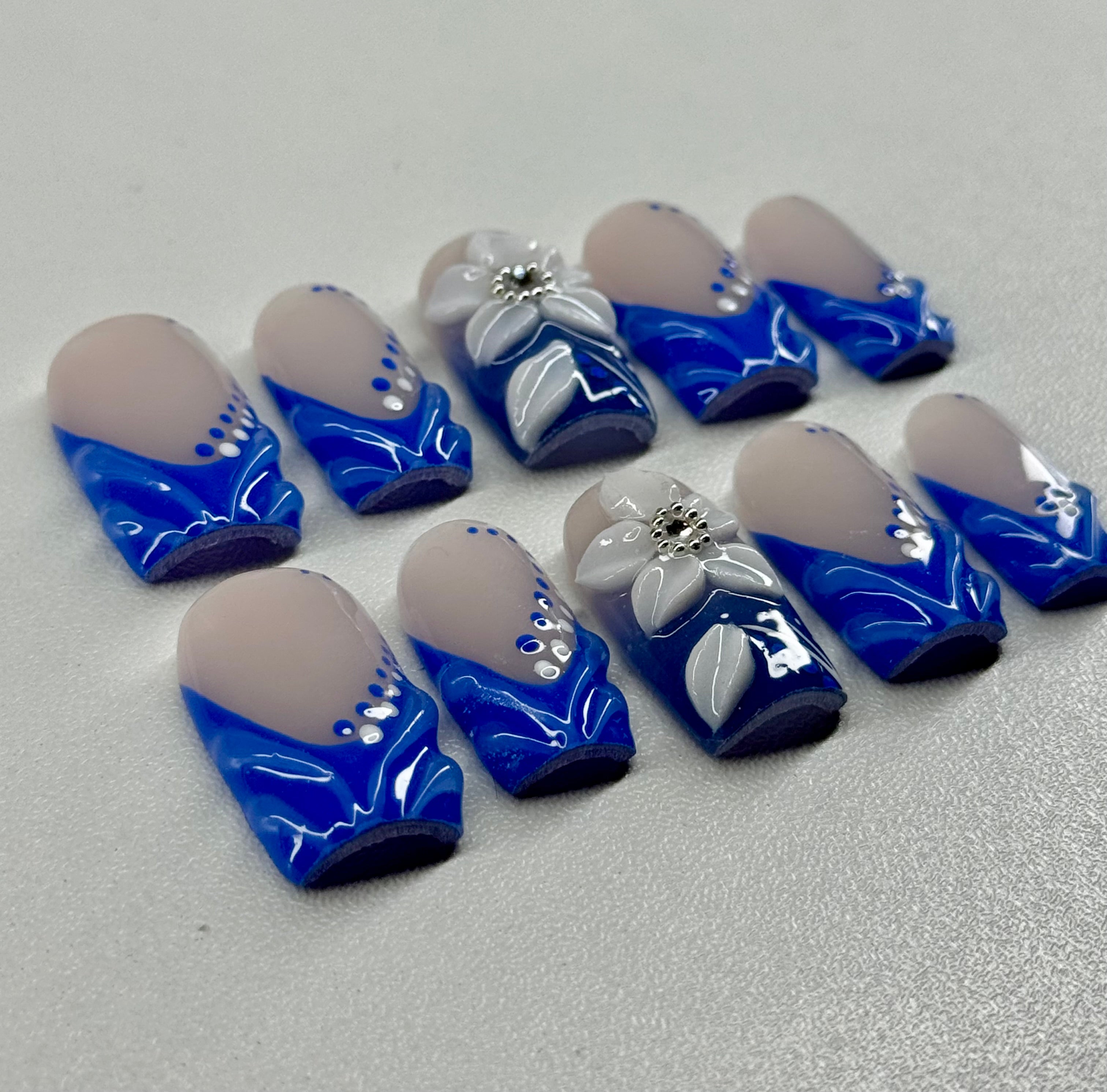 Set of blue and white floral nail art designs on a nude surface