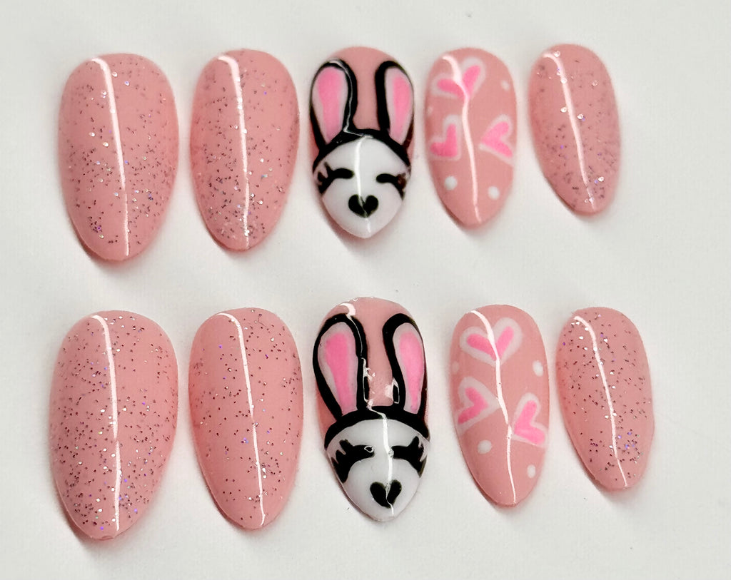 Set of pink glittery nails with bunny face designs on a white background
