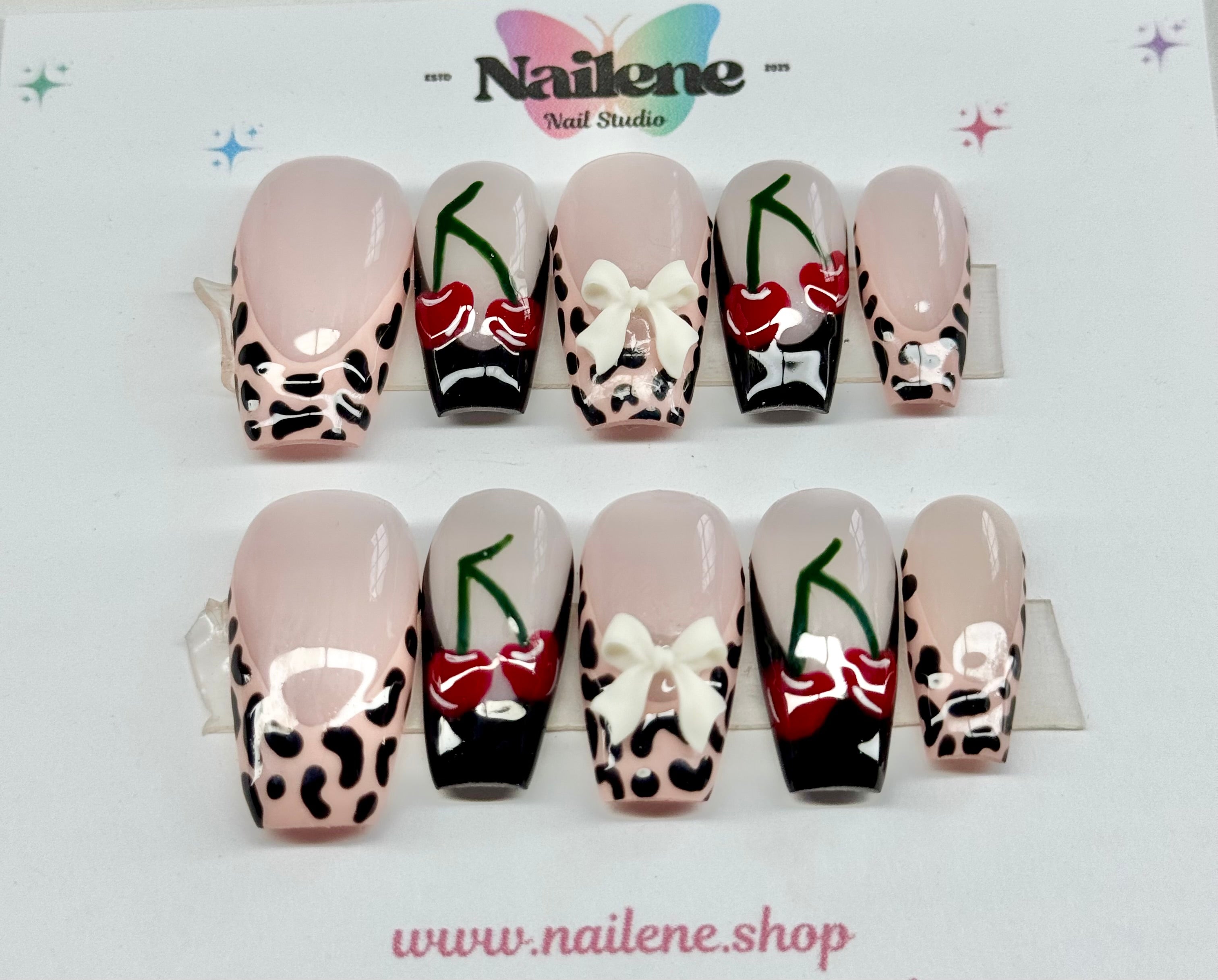 Decorative false nails with animal print, bow, and cherry designs on a white background with 'Nailene' branding.